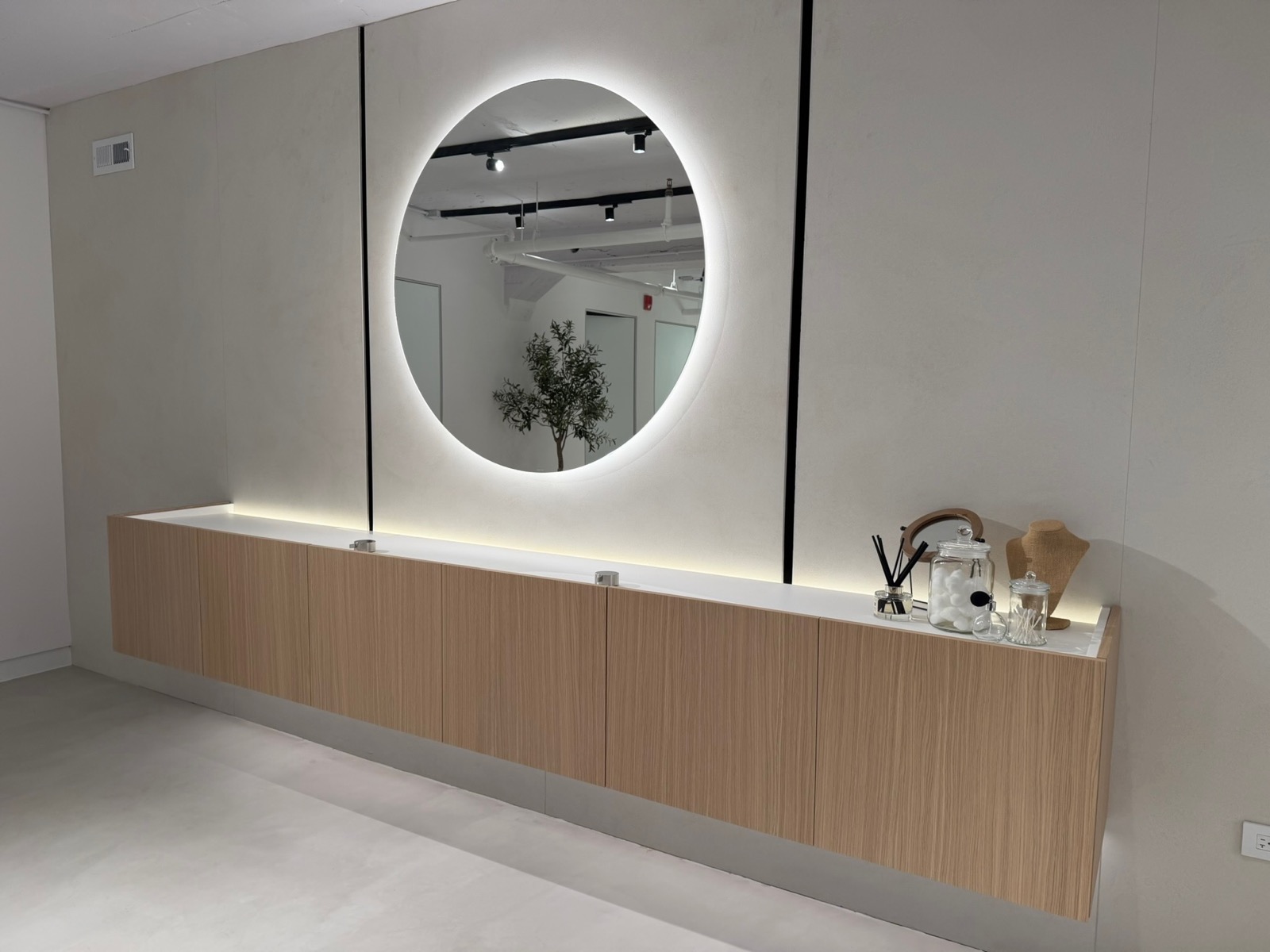 A floating oak vanity beneath a round backlit mirror